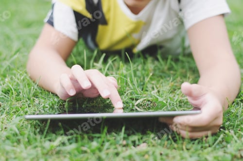 Preview: A kid using iPad lying on the green grass backyard relaxing gaming having fun happiness vacations