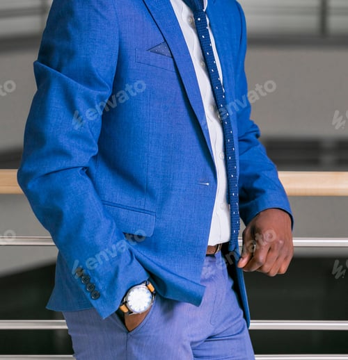 Preview: Vertical shot of a male wearing a blue suit with a white shirt, tie, watch, and blue trousers