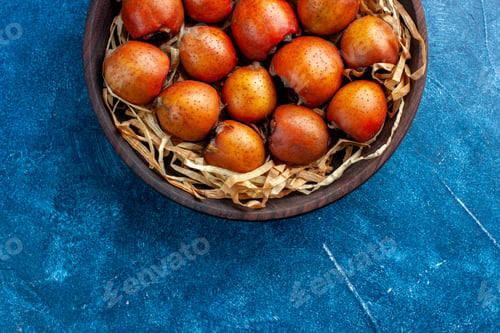 Preview: Half shot of mespilus germanica in a tissue basket in a brown bowl on the top on blue background