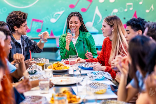 Preview: Multiethnic friends enjoying meal and drinks together in a restaurant