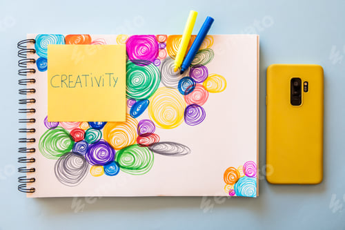 Preview: Top view of a modern mobile phone next to a drawing of colorful spirals with markers and a note