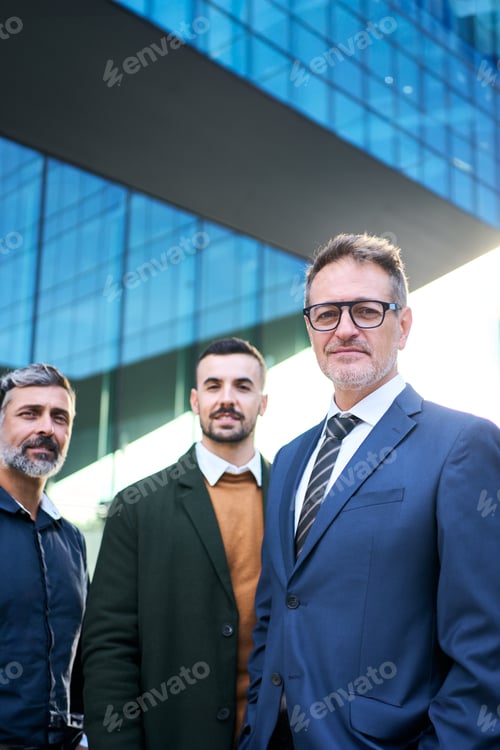 Preview: A group of men in suits, sharing a smile, stand in front of a building