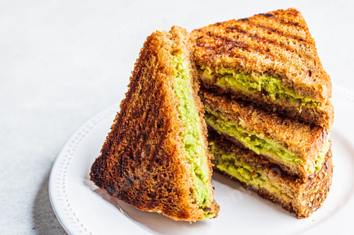 Preview: Grilled avocado and cheese sandwiches on white plate.