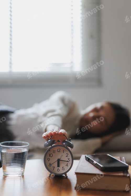 Preview: Woman turning off alarm clock in bedroom, early morning wake up