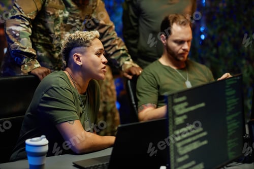 Preview: Young female military officer sitting by workplace among male colleagues
