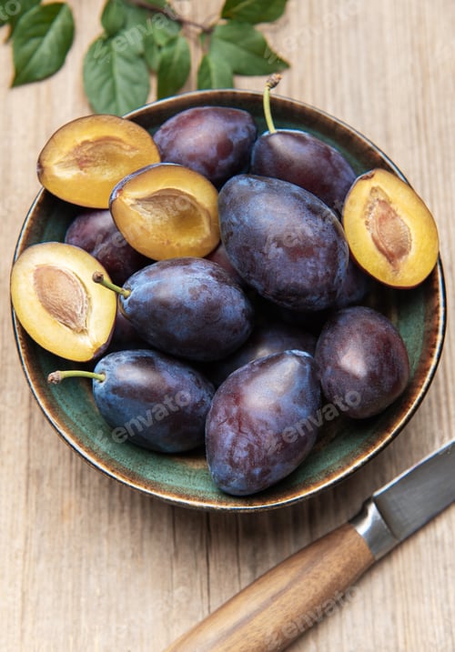 Preview: Fresh ripe plums in bowl on wood surface