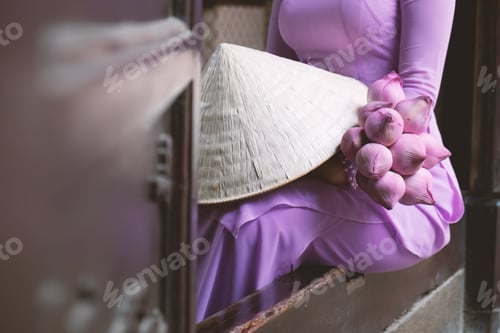 Preview: A woman in traditional Vietnamese dress sitting with a bunch of pink lotuses on her lap