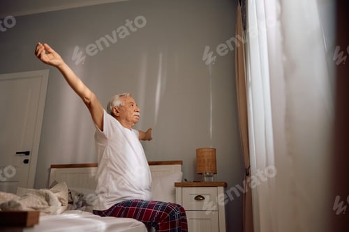 Preview: Senior man stretching on a bed in the morning.