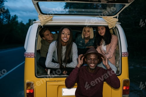 Preview: multiethnic friends traveling together on retro minivan at evening