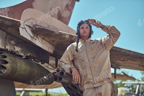 Preview: Mechanic in uniform and flying helmet standing near an old war fighter-interceptor