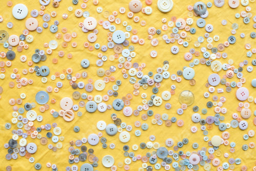 Preview: top view of scattered colorful buttons on yellow cloth background