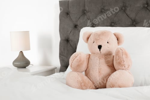 Preview: Cute teddy bear sitting on bed indoors. Space for text