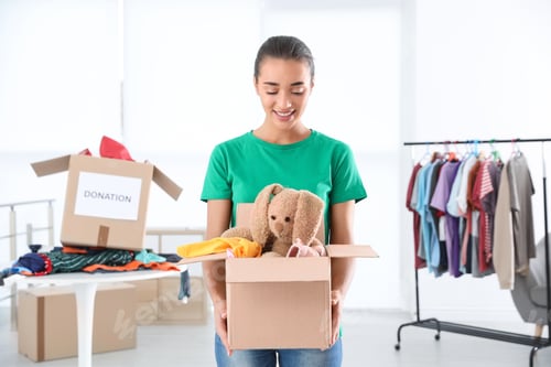 Preview: Young woman holding box with donations indoors