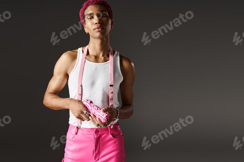 Preview: handsome african american man in vibrant outfit with suspenders and accessories posing with toy gun
