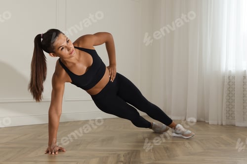 Preview: Young woman doing side plank exercise at home