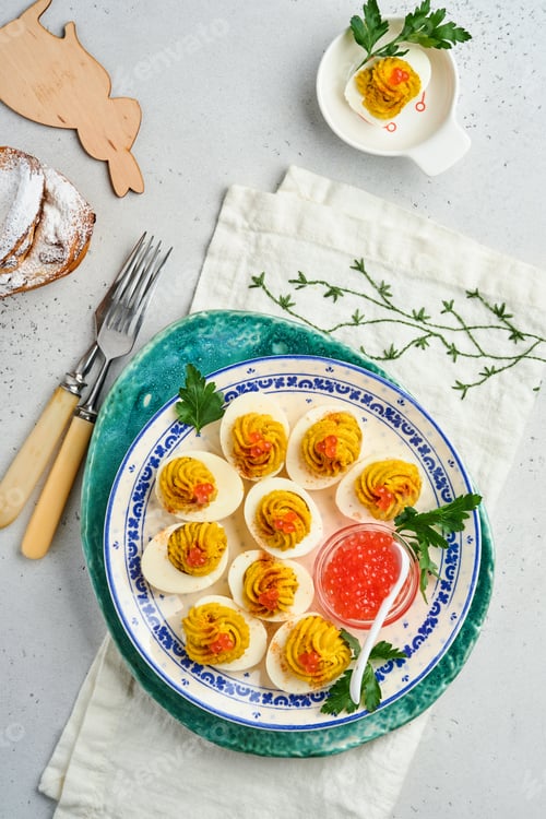Preview: Stuffed eggs with red caviar and paprika on plate for appetizer easter table, top view, copy space.