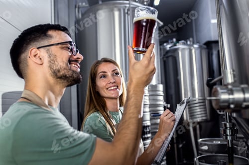 Preview: Man and woman working in craft brewery examining quality of the beer.
