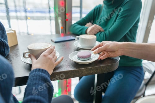 Preview: Close-up of two women hands with cups of coffee and macaroons on plate