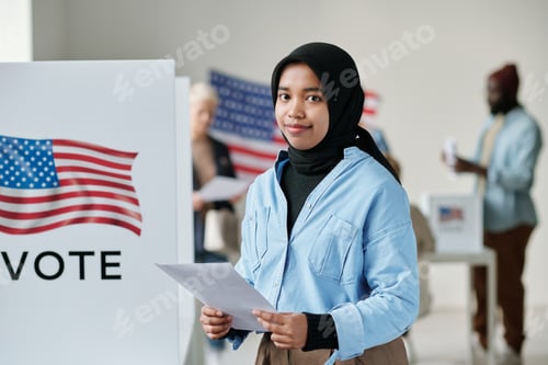Preview: Young smiling Muslim woman in hijab holding ballot paper