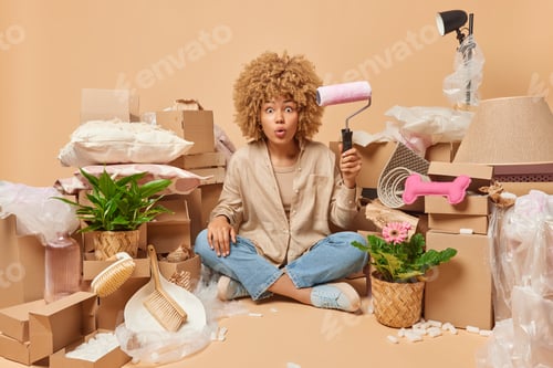 Preview: People and relocation concept. Surprised woman sits crossed legs on floor around cardboard boxes hol