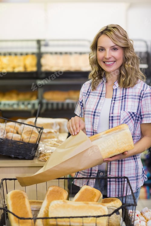 Preview: Female baker wrapping rectangular loaf in brown paper behind bakery counter with wicker baskets