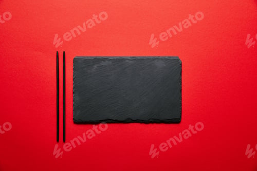 Preview: top view of empty black slate plate for sushi and chopsticks isolated on red