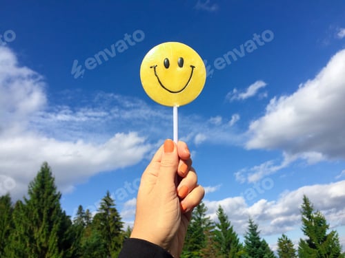 Preview: Woman’s hand holding smiley face candy with blue sky in the background