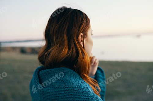 Preview: red-haired woman in the mountains with a blue plaid on her shoulders back view