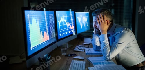 Preview: Frustrated businessman with computer sitting at desk, working late. Financial crisis concept