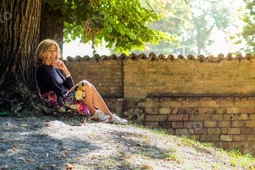 Preview: senior fit happy lady relax sit next to tree in park wear floral skirt and black long sleeve shirt