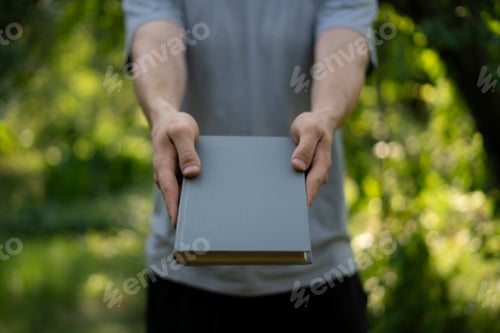 Preview: A person extends their hands to share a book in a tranquil outdoor environment