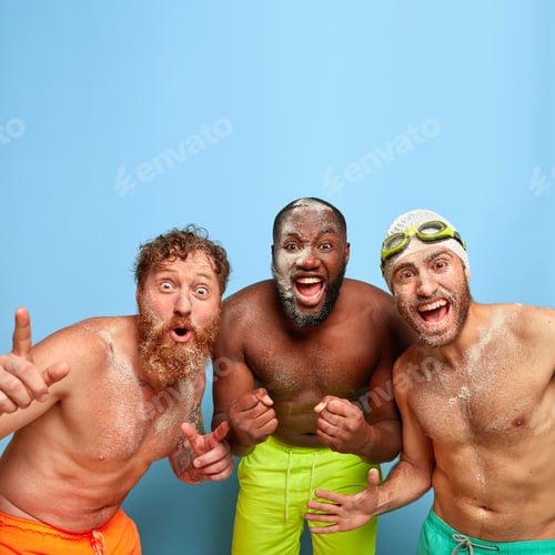 Preview: Excited happy mixed race male friends clench fists with joy, have fun and throw sand on each other,