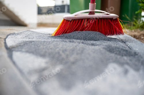 Preview: Broom brushing filling sand into the gaps between newly layed concrete tiles to finish the project