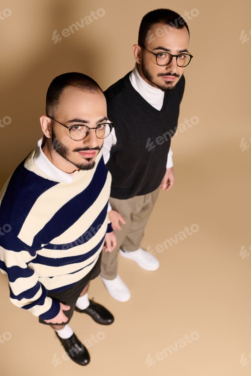 Preview: Stylish twin brothers pose confidently against a neutral backdrop showcasing their unique fashion