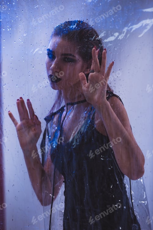 Preview: Fashionable model with wet hair dressed in black swimming suit and transparent rain coat is posing