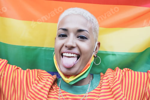 Preview: Young lesbian woman smiling on camera while holding LGBT rainbow flag