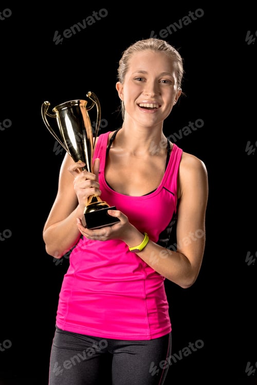 Preview: Happy sportswoman with trophy celebrating victory and looking at camera