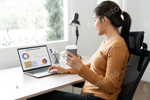Preview: Woman analyzing financial data graphs, charts on laptop display at a modern home workspace.
