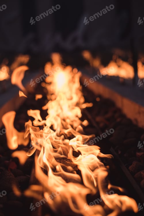 Preview: Closeup of a charcoal grill with burning embers, set against a backdrop of gray rocks and pebbles