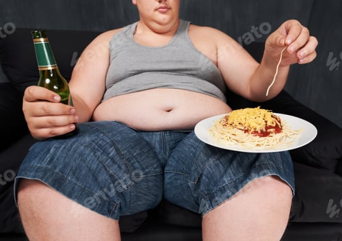 Preview: A cropped shot of an obese young man sitting on a sofa and eating spaghetti with his hands