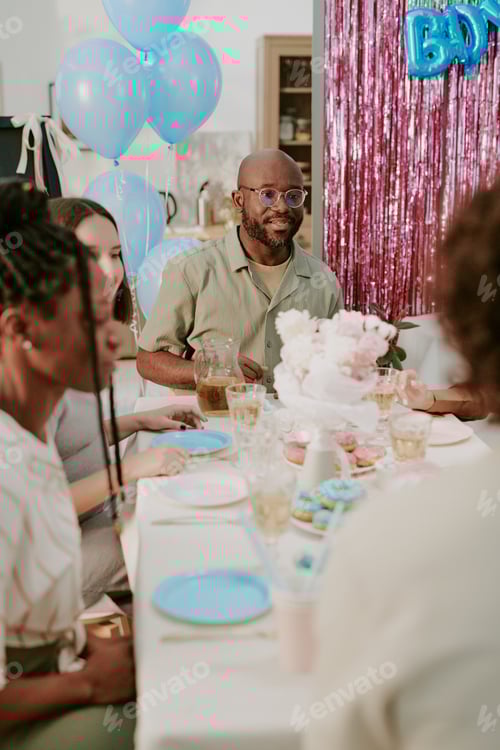 Visualização: Homem negro de meia idade comemorando chá de bebê com um grupo diversificado na mesa