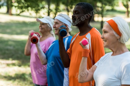 Preview: selective focus of african american man exercising with dumbbells with pensioners in park