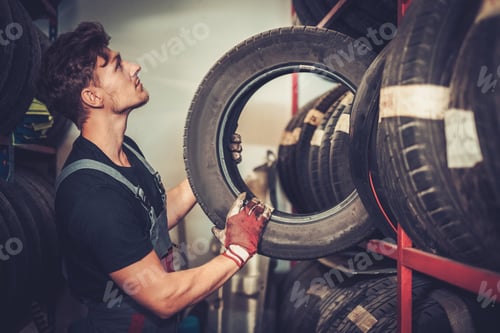 Preview: Professional car mechanic choosing new tire in auto repair service.