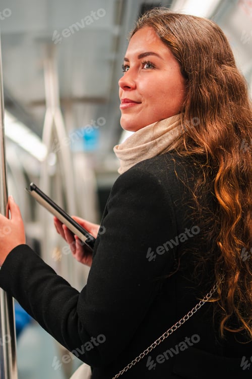 Preview: Young woman engaged in reading an e-reader while standing in a subway train
