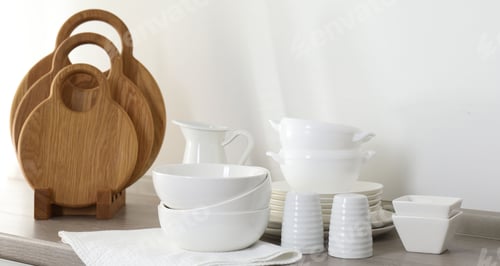 Preview: Different clean white dishware and wooden cutting boards on counter in kitchen