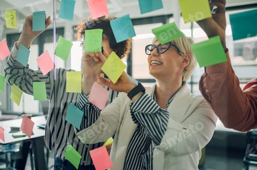 Preview: Multiracial team at work writing ideas on sticky notes on the glass wall