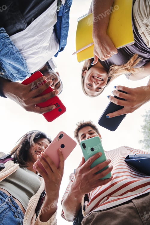 Preview: Vertical low angle view of multiracial group of young friends enjoying and smiling using their