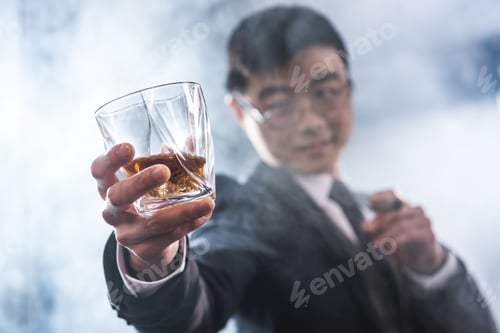Preview: Close-up view of confident asian businessman drinking whiskey and smoking cigar