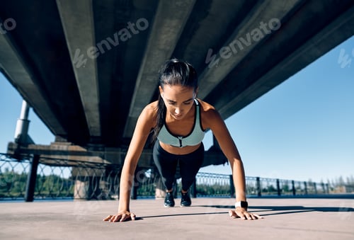 Preview: Young athletic woman doing push ups outdoors in urban city background