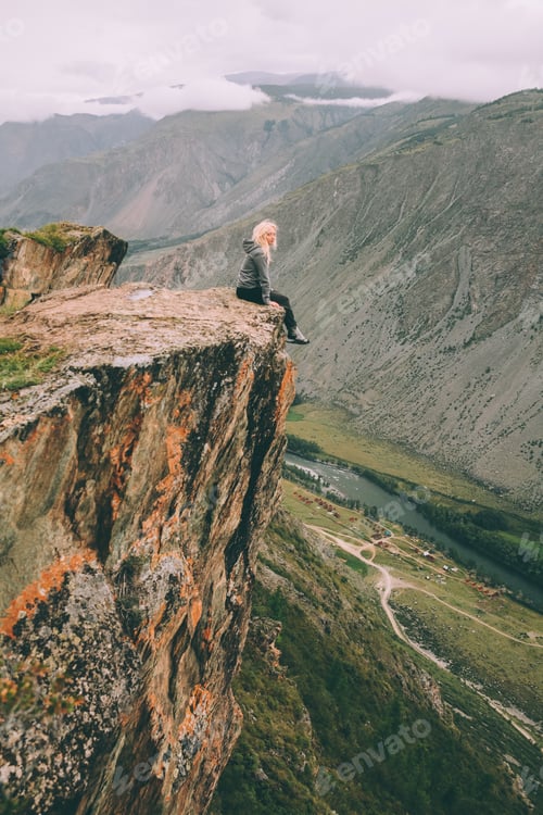 Preview: young woman sitting on cliff and looking at majestic mountains in Altai, Russia